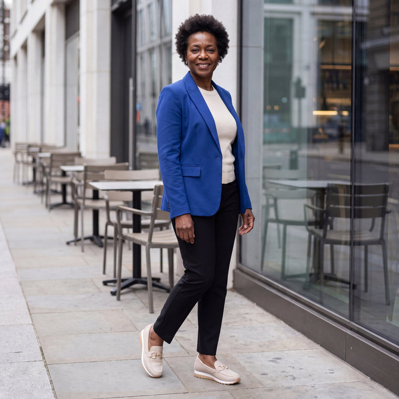 Black British woman wearing beige woven Lili loafers beside a modern London café