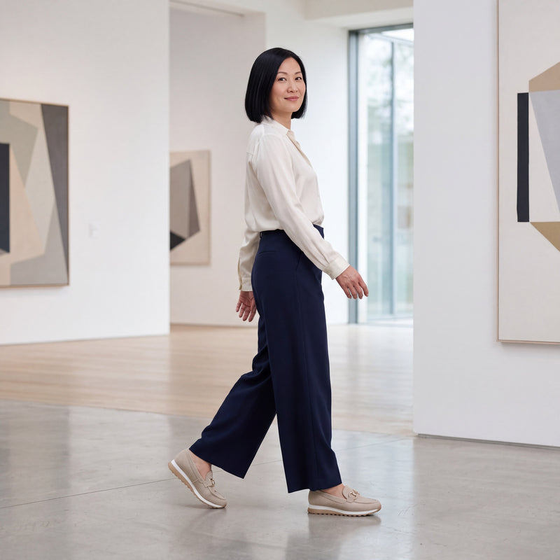 British East Asian woman walking in beige woven Lili loafers through a modern gallery