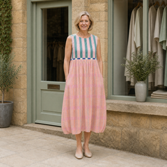 Helen models the pink and teal striped Lily pastel midi dress in a front full-body view outside a pale-stone Cotswold boutique.
