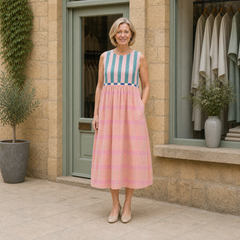 Helen models the pink and teal striped Lily pastel midi dress in a contextual full-body view outside a pale-stone Cotswold boutique.